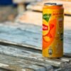 Orange iced tea can placed on weathered wooden table outdoors in warm sunlight.