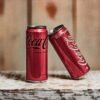Close-up product shot of Coca-Cola cans against a rustic wooden background.