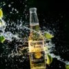 Dynamic image of Corona beer bottle with lime and water splash against a black background, evoking refreshment.