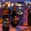 Two Sagres beer bottles on a table with a bokeh backdrop of Lisbon's city lights at night.